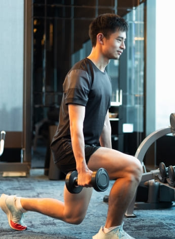 The photo is of a man in a gym doing lunges while holding weights. 